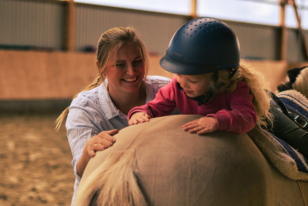 Ein Kind streichelt während einer Reittherapie Einheit über den Rücken des Pferdes